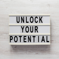 'Unlock your potential' on a lightbox on a white wooden background, top view. Flat lay, overhead, from above.
