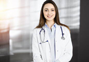 Smiling young woman-doctor is standing in sunny clinic indoors