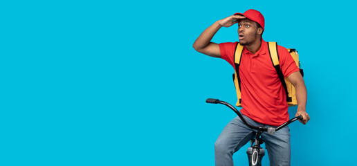 Surprised black delivery man riding bicycle looking at copyspace