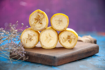 Side view of natural grown split fresh bananas on wooden cutting board on blue background