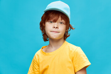 Red-haired boy in a cap pursed his lips in a yellow t-shirt blue background 