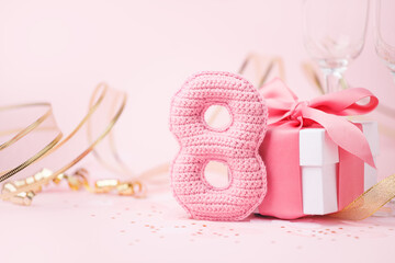 8 March, International Women's Day concept. Figure eight of pink crochet with luxury gift box, big bow on pink background. Space for text, monochrome seasonal holiday greeting card