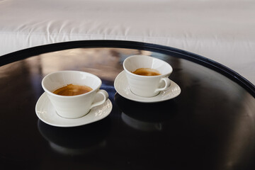 Defocused Two white coffee cups on a table with blurred balcony partition light background
