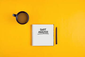SWOT analysis written on notebook with pen and coffee mug on yellow background. Marketing strategy.