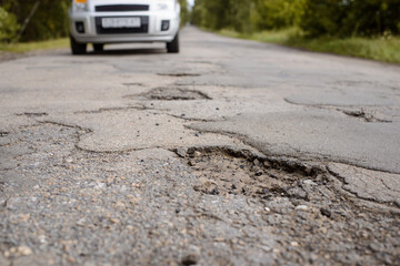 Damaged road and approaching car on the background. Concept of road in bad condition.