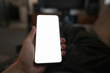 Man hold smartphone with white screen in his hand lying on a couch in home environment