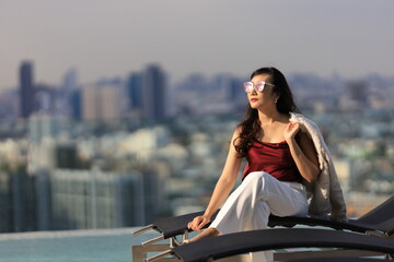 Luxury Asian CEO woman entrepreneur sitting on the rooftop looking to the sun with skyscraper and cityscape on the background with copy space
