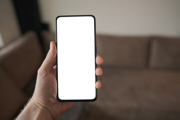 Man hold smartphone with white screen in his hand standing indoors in home environment