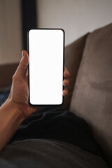 Man hold smartphone with white screen in his hand lying on a couch in home environment