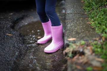 Young girl child wearing pink gumboots on the grass outdoors on rainy day