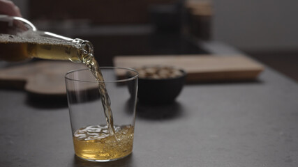 apple cider pour in glass and pistachios in black bowl on concrete countertop