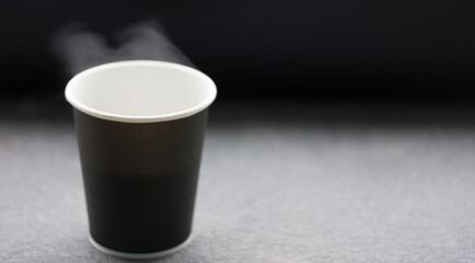 A disposable cup of hot coffee or tea. Colors - black, white. Hot steam cloud.