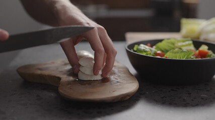 man hands slicing mozzarella on wood board on home kitchen