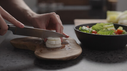 man hands slicing mozzarella on wood board on home kitchen
