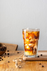 Cold refreshing coffee with ice and creamy clouds in a glass on a wooden board close-up, cocoa beans in coconut shell