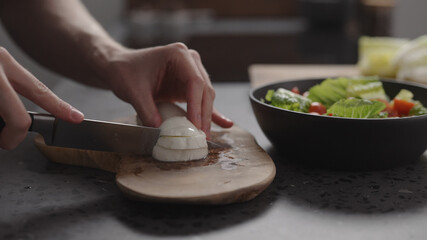 man hands slicing mozzarella on wood board on home kitchen