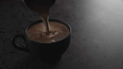 pour hot chocolate into black cup on concrete countertop with copy space under dim light