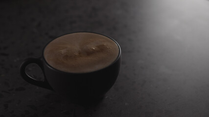 hot chocolate into black cup on concrete countertop with copy space under dim light