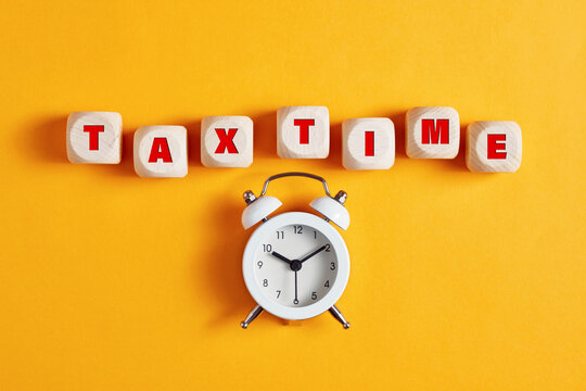 The word tax time written on wooden cubes with an alarm clock. Tax payment reminder concept.
