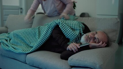 Caring daughter covering aged father, sleeping on sofa in front on tv, family