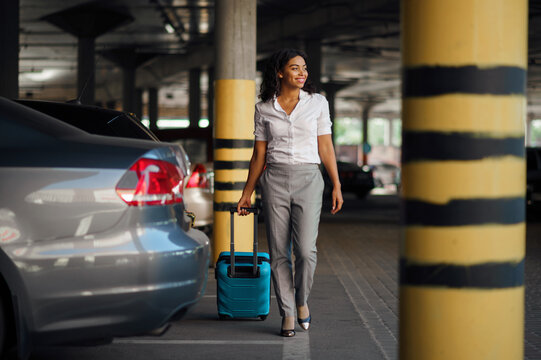 Young woman with suitcase in car parking