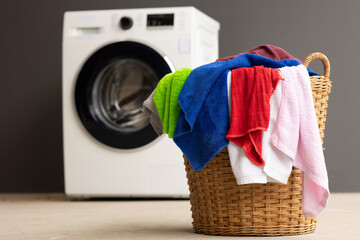 Piles of laundry in the basket and the washing machine are placed close to each other.