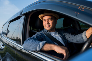 Naklejka premium A young Asian man drives a car on a clear day. With beautiful blue sky. He driving to travel by car.