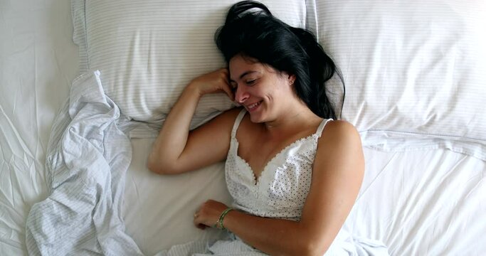 Happy woman in 30s lying in bed in the morning smiling, top view