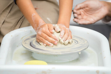 Hands of a little girl who sculpts a craft on a potter's wheel with the help of her mother