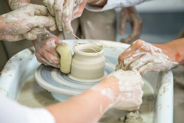 Trimming a clay pot with a thread on a potter's wheel in a gonsar's workshop