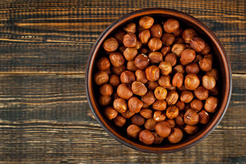 Hazelnuts in a clay bowl on an old shabby board. Nuts on a brown wooden table.