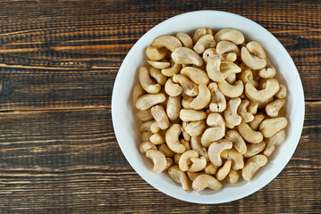 Cashews in a white bowl on an old shabby board. Nuts on a brown wooden table.