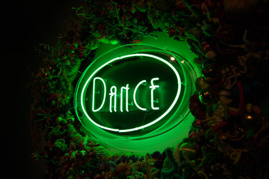 Green neon dance sign against dark background - Powered by Adobe