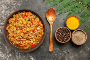 top view roasted eggplant salad in bowl wooden spoon different spices in small bowls on dark background