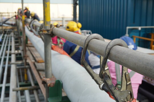 Hook of safety harness on scaffolding pipe during working at heights in construction site, Chemical plant.