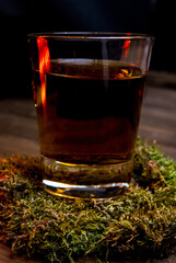 a glass of whiskey  with moss on a wooden table 