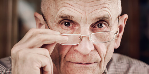 mature pensioner adjusts spectacles by hand in light room closeup