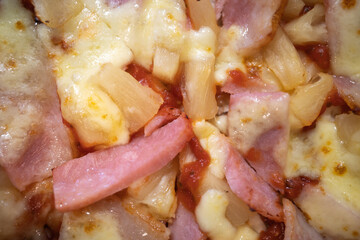 Closeup surface of pizza sprinkle with pieces of ham, bacon and cheese and some of pineapple