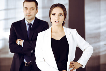 Young beautiful businesswoman is standing in an office with a male colleague at the background. Concept of success in a business