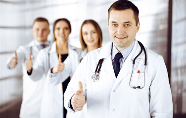 Group of professional doctors are standing as a team with thumbs up in a hospital office, ready to help their patients. Medical help, insurance in health care and medicine concept