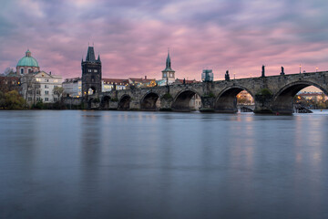 Charles Bridge on the Vltava River at sunset and colorful clouds and lights on the bridge in the early evening in the center of Prague