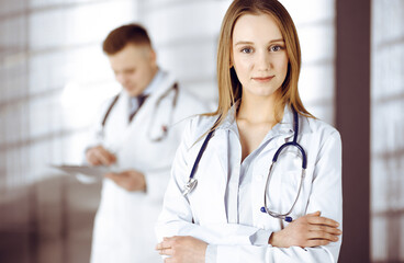 Professional beautiful woman-doctor with a stethoscope is standing with crossed arms in a clinic. Young doctors at work in a hospital. Medicine and healthcare concept