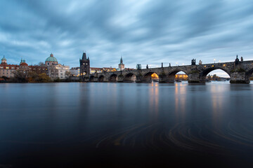 Charles Bridge on the Vltava River at sunset and colorful clouds and lights on the bridge in the early evening in the center of Prague