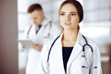 Portrait of a professional friendly woman doctor with a stethoscope, standing with a colleague in a clinic. Young doctors at work in a hospital. Medicine and healthcare concept