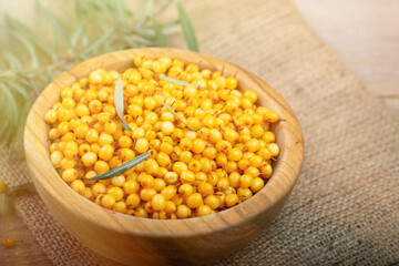 Sea buckthorn. Fresh ripe berry in wooden bowl with leaves on wood background.