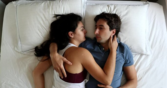 Married millennial couple in bed, people communication, wife listening to husband while they cuddle