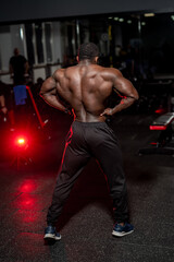 Fototapeta na wymiar Strong back of muscular bodybuilder poses to the camera in modern gym with dark light. Bodybuilding, posing, health, fitness, beauty.