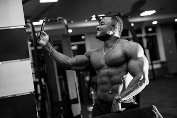 Fototapeta na wymiar Strong muscular african american man makes selfie on gym background. Black and white photo.