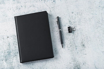 Office desk with black notepad and pen on gray background.