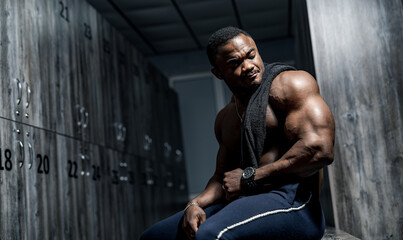 Muscular african male in locker room. Man having rest after heavy training. Portrait of bodybuilder.